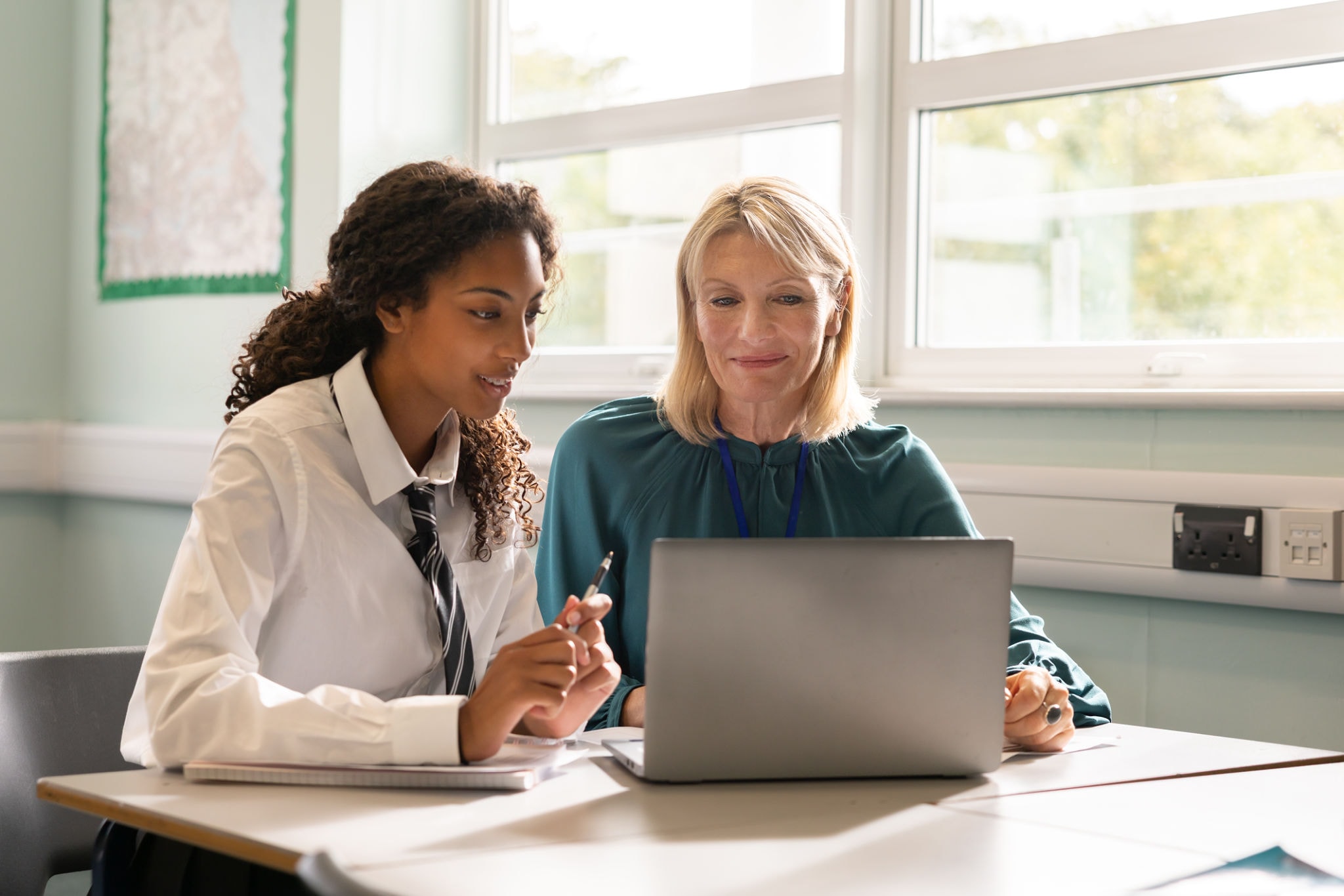 Teacher and student collaborating at a laptop in a classroom